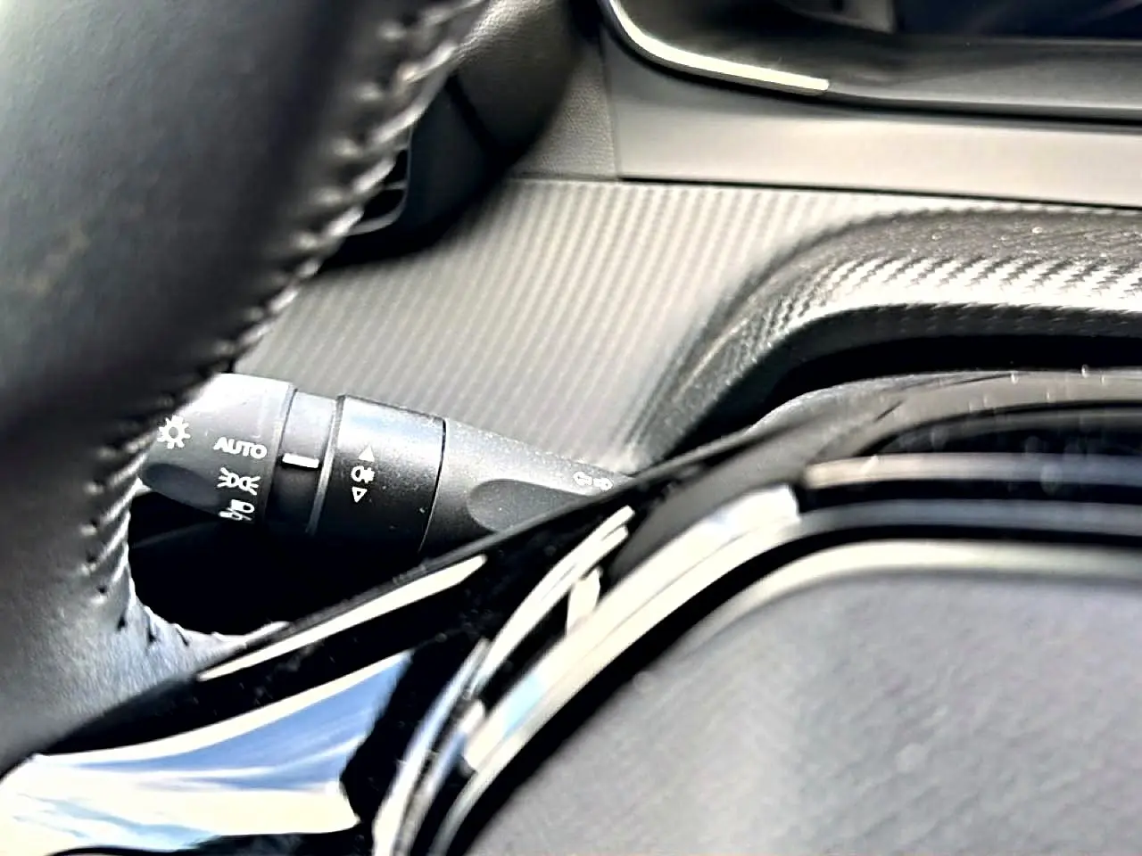 Gros plan sur le volant noir et la commande des phares du Peugeot 2008 1.2 100 Allure gris Artense, intérieur moderne.