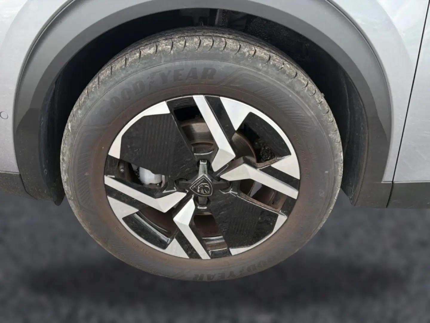 Gros plan sur la roue avant gauche du Peugeot 2008 gris Artense avec jante alu bicolore et logo lion central.