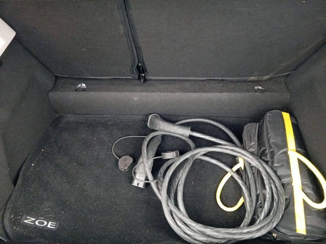Coffre ouvert d’une Renault ZOE électrique 2022, vue intérieure montrant un câble de recharge et un sac noir avec liseré jaune.