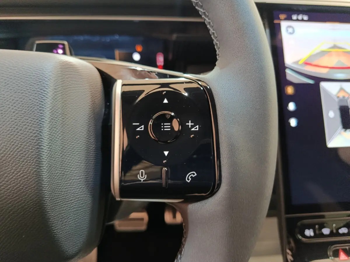 Gros plan sur les commandes multifonctions noires à gauche du volant cuir gris du Citroën C5 Hybride 2026.