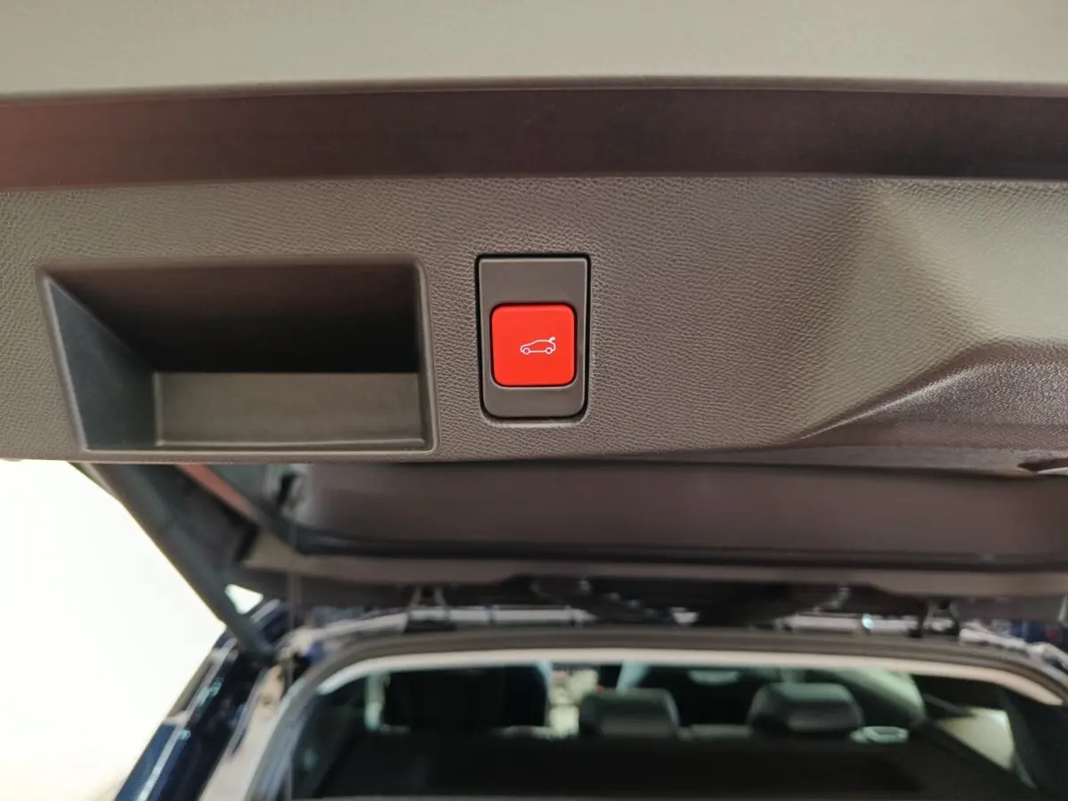 Bouton rouge d'ouverture électrique du coffre sur la porte arrière d'une Citroën C5 hybride bleue vue de l'intérieur du coffre.