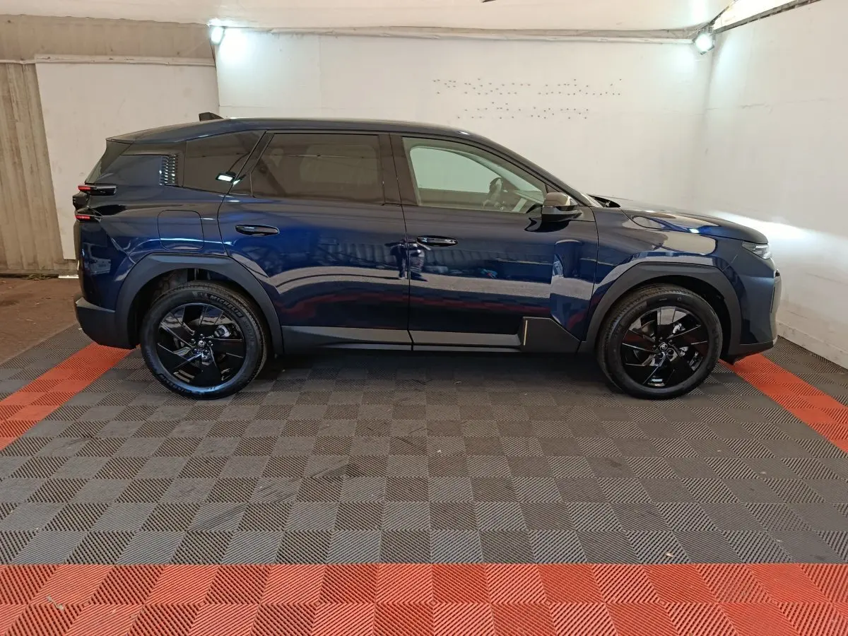 Profil côté droit d'une Citroën C5 hybride bleu foncé avec jantes noires, dans un garage éclairé.