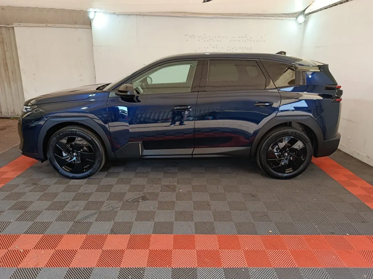 Vue latérale droite d’un Citroën C5 hybride bleu foncé avec jantes noires et toit noir dans un garage.