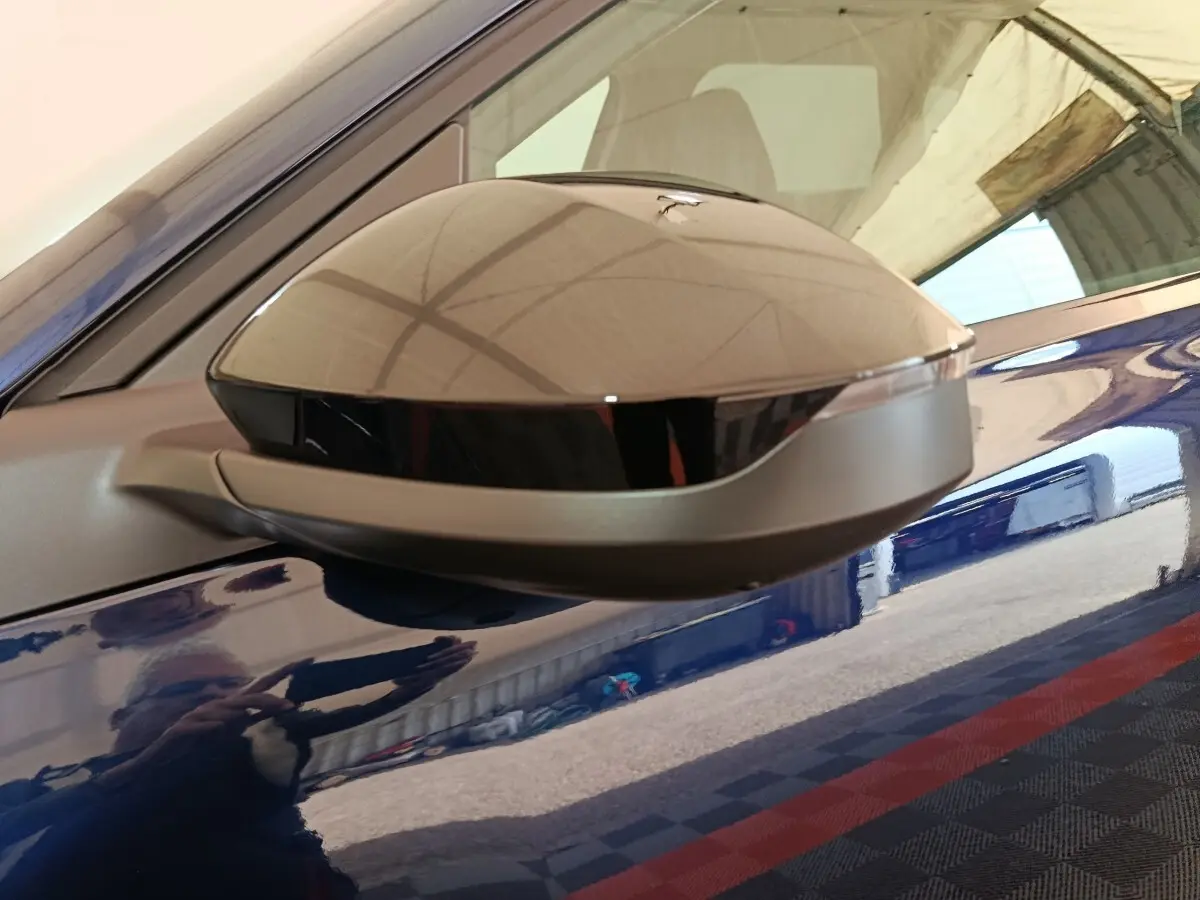 Gros plan sur le rétroviseur droit gris et noir du Citroën C5 hybride bleu, reflétant l'environnement intérieur.