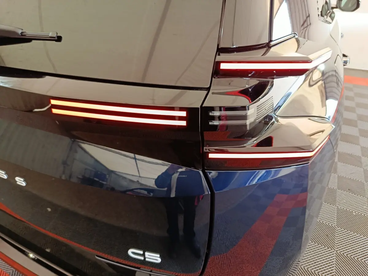 Gros plan sur l'arrière droit bleu du Citroën C5 hybride 2026, mettant en valeur les feux LED horizontaux distinctifs.