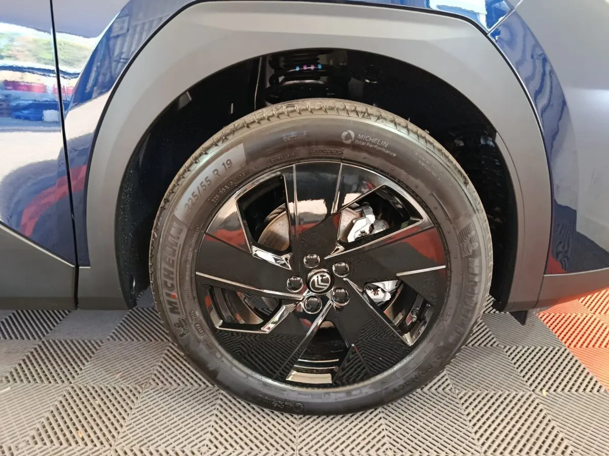Gros plan sur la roue arrière droite noire brillante d'une Citroën C5 hybride bleu 2026 avec jante design et pneu Michelin.