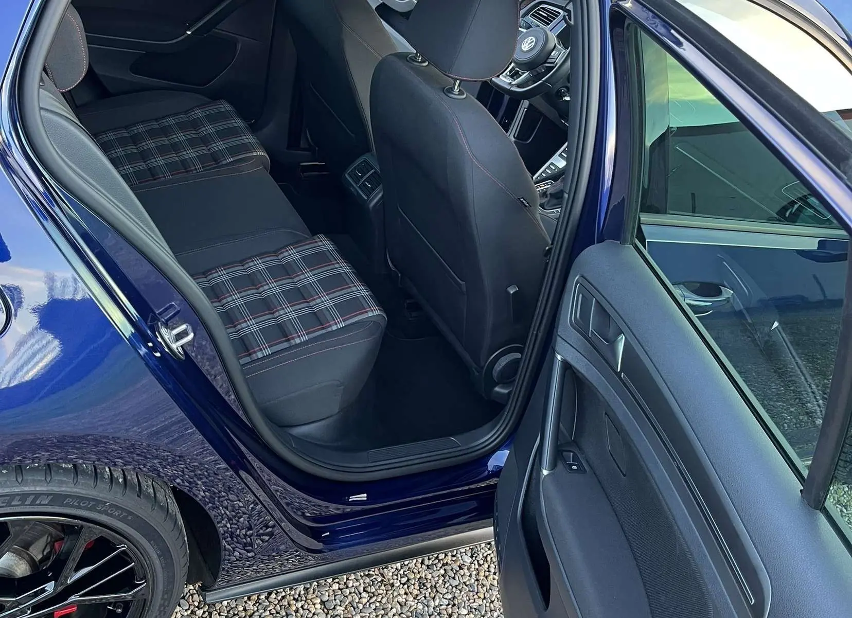 Vue intérieure côté arrière gauche d'une Volkswagen Golf VII GTI Performance bleu lapiz, sièges à motif tartan et volant visible à l'avant.