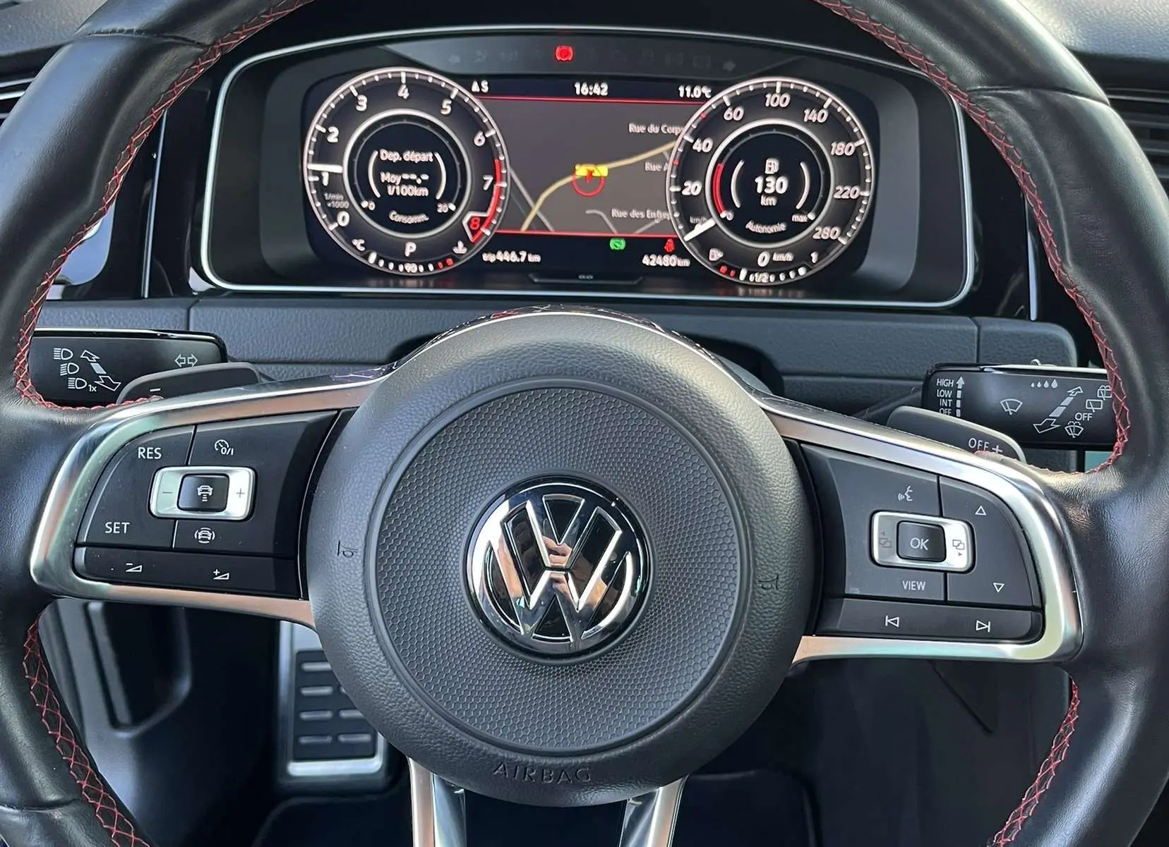 Vue rapprochée du volant cuir noir avec surpiqûres rouges et tableau de bord numérique d'une Volkswagen Golf GTI Performance.