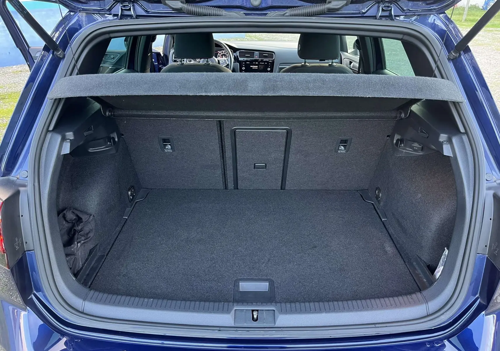 Coffre ouvert d'une Volkswagen Golf VII GTI Performance bleu lapiz metal, vue arrière montrant l'espace de chargement et l'intérieur.