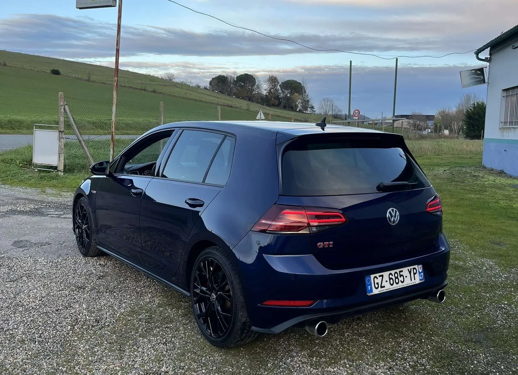 Volkswagen Golf VII GTI Performance bleu lapiz métal vue 3/4 arrière droit sur un chemin gravillonné.