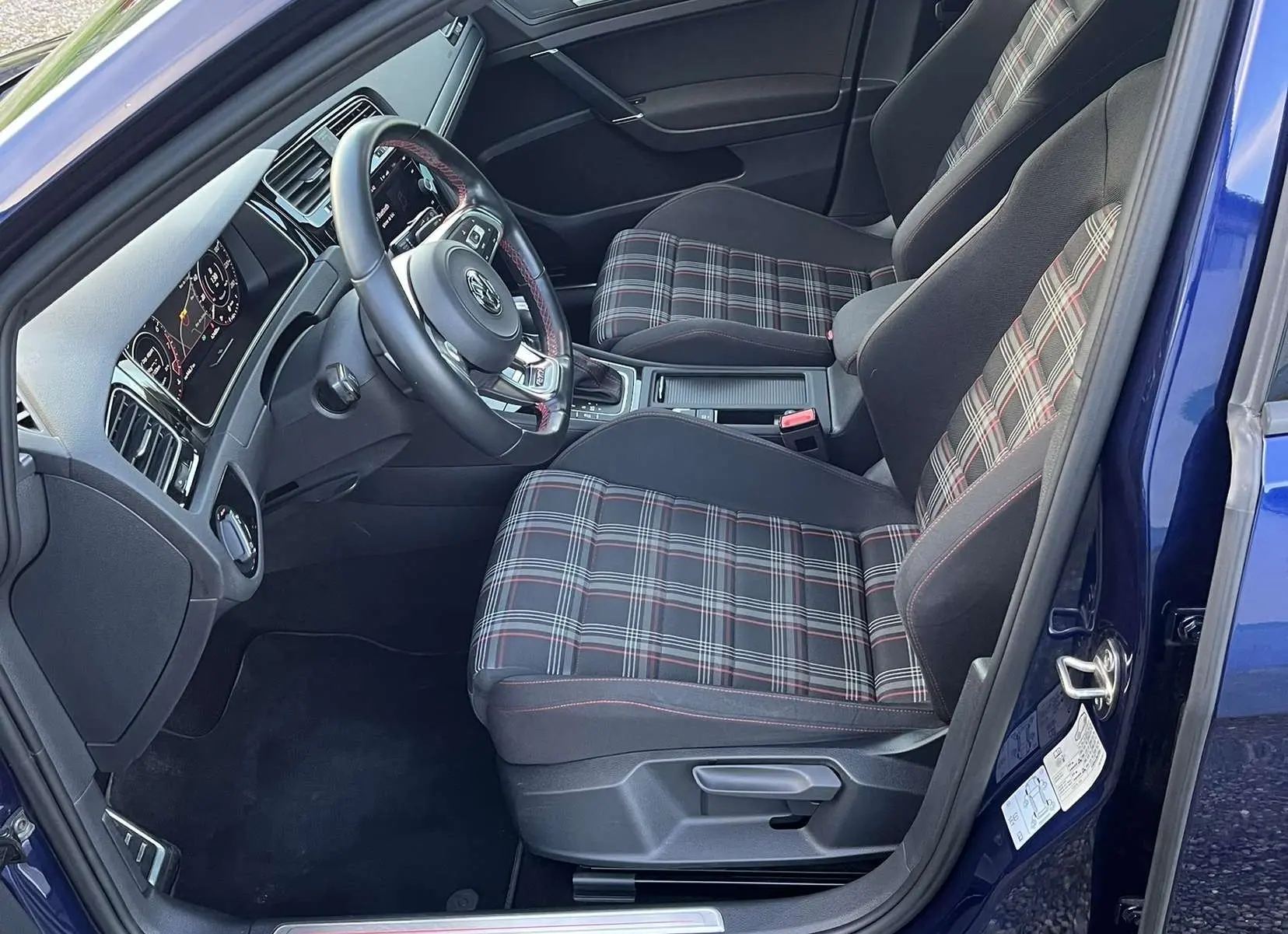 Intérieur côté conducteur d'une Volkswagen Golf VII GTI Performance bleu lapiz, sièges à motif tartan et volant cuir.