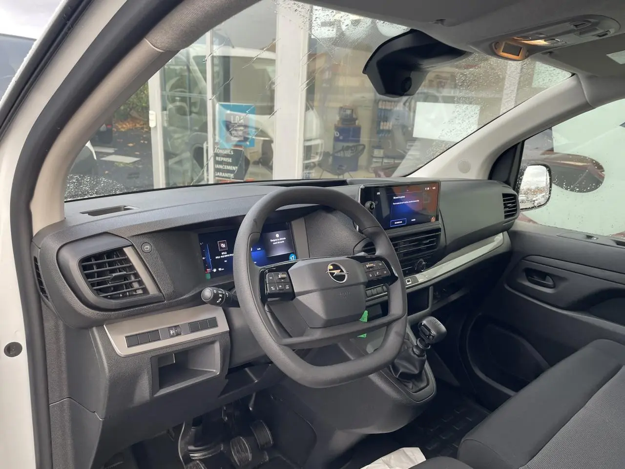 Intérieur avant droit de l'Opel Vivaro blanc 2024, volant multifonction, écran tactile et levier de vitesses manuel visibles.