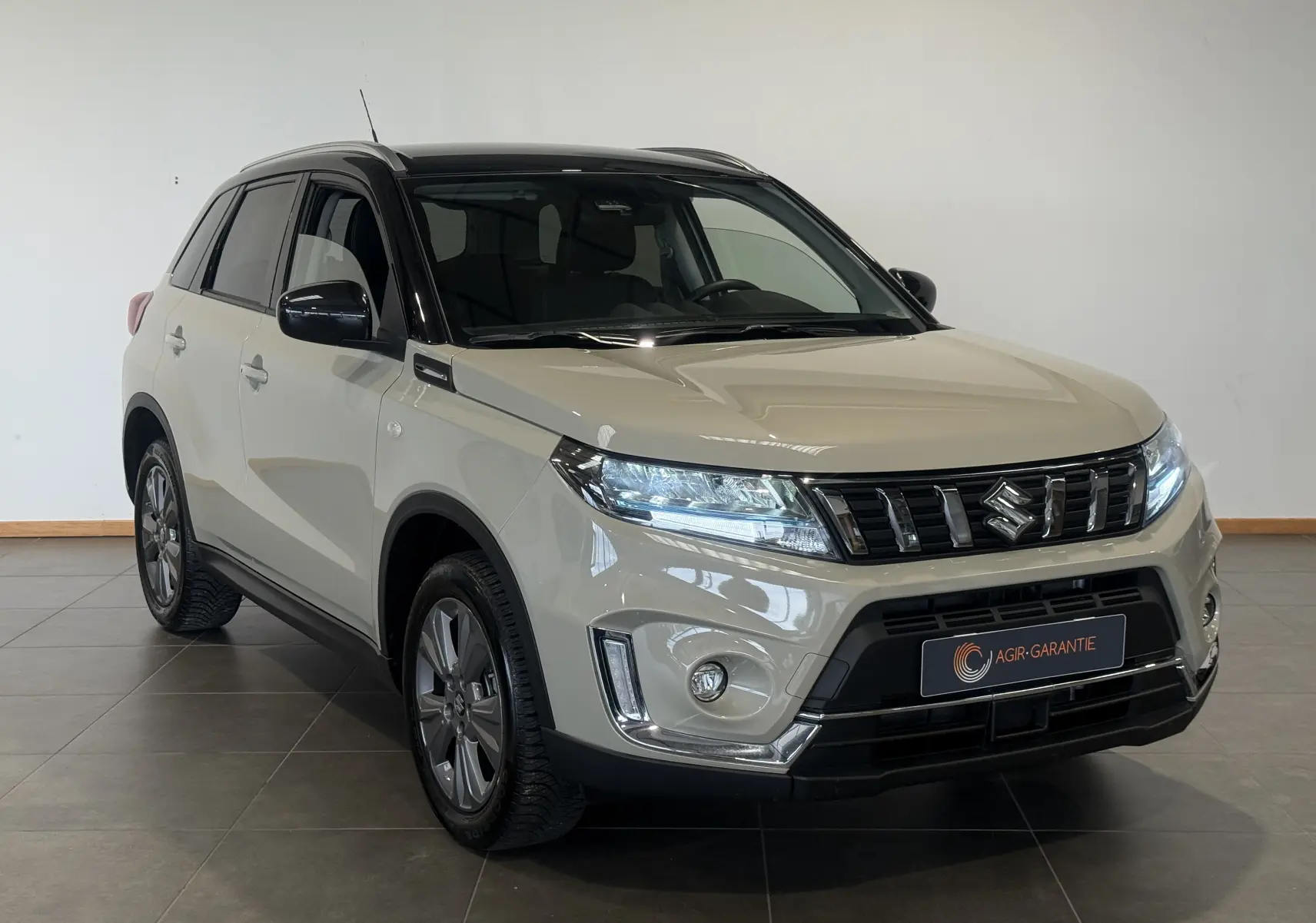 Suzuki Vitara beige 2023 vue 3/4 avant droit avec toit noir et calandre chromée dans un showroom.