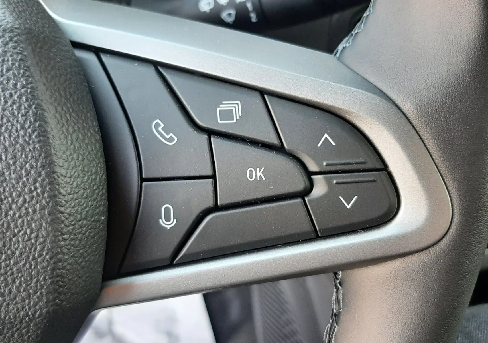 Gros plan sur les commandes multifonctions à gauche du volant du Dacia Duster 2025, finition Sandstone.