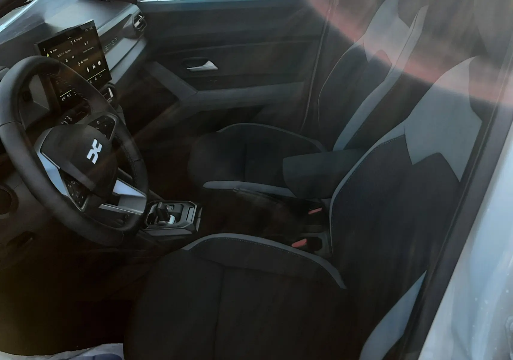 Vue intérieure côté conducteur du Dacia Duster 2025, sièges tissu gris et noir avec tableau de bord moderne.