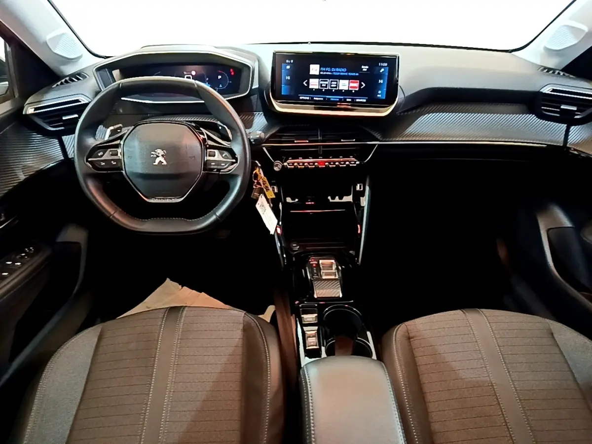 Vue intérieure avant de la Peugeot 208 2023, tableau de bord moderne avec écran tactile central et volant multifonctions cuir.