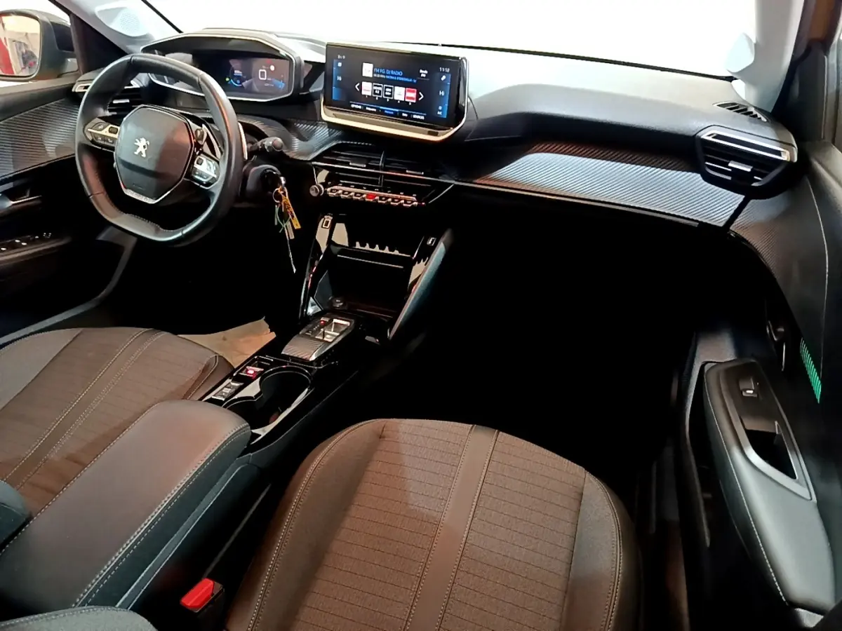 Vue intérieure avant droite du Peugeot 208 jaune 2023, montrant le volant cuir, écran tactile central et console moderne.