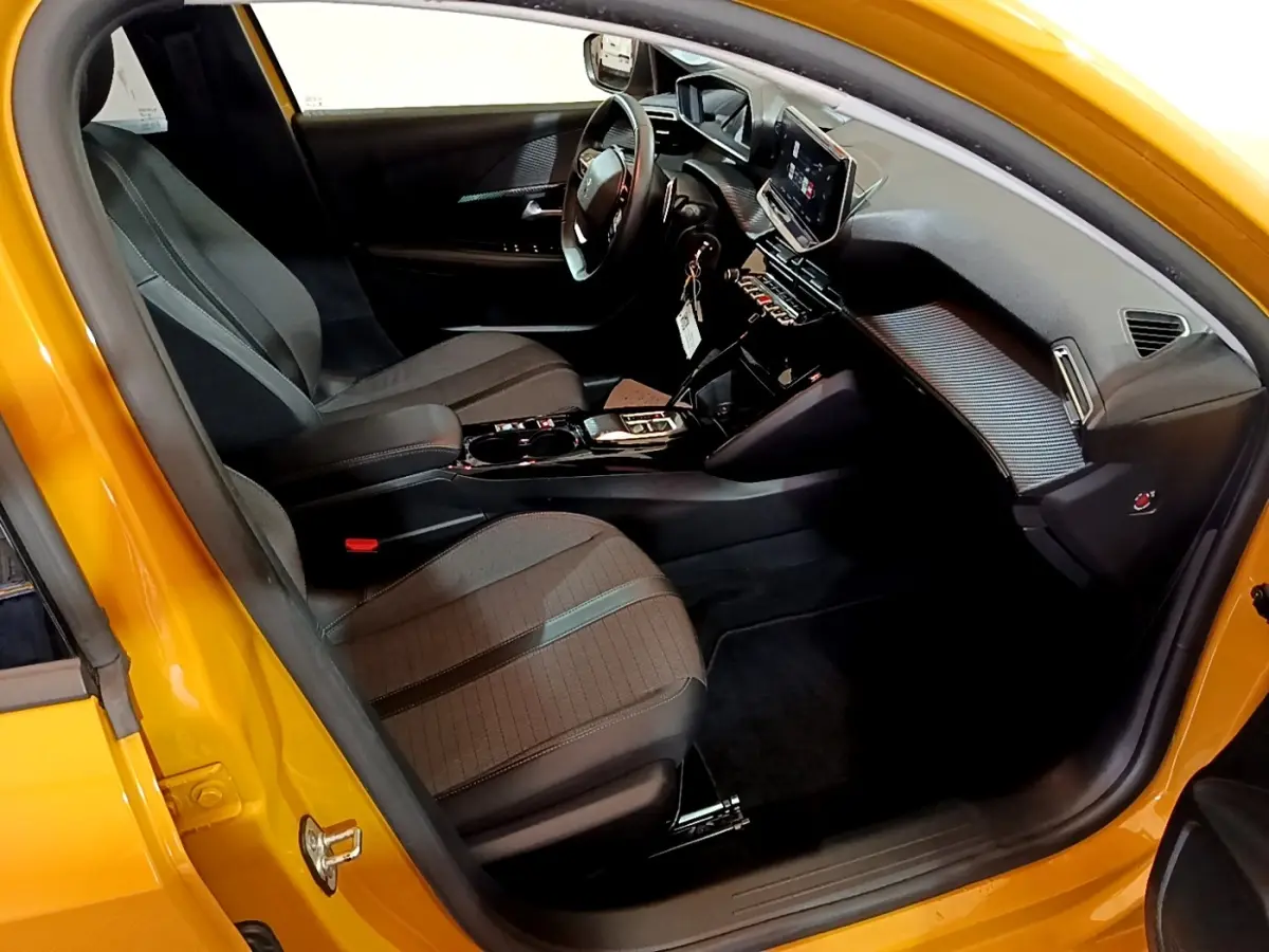 Vue intérieure côté conducteur de la Peugeot 208 jaune 2023, avec tableau de bord numérique et sièges noirs.