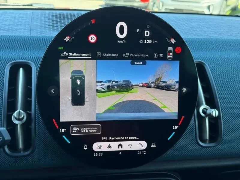 Vue rapprochée de l’écran circulaire du tableau de bord du MINI Countryman 2024 affichant la caméra avant et les aides au stationnement.