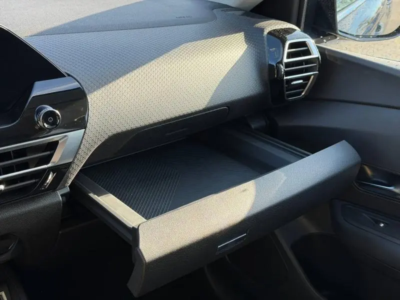 Vue intérieure côté passager du tableau de bord noir du Citroën C4 X 2024 avec boîte à gants ouverte et aérateurs visibles.