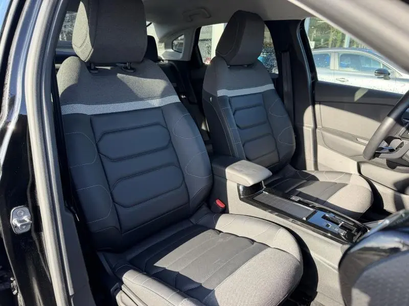 Vue intérieure côté conducteur et passager avant du Citroën C4 X 2024 noir, sièges bi-matière gris et noir avec console centrale.
