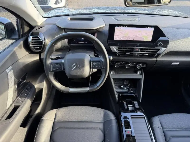 Vue intérieure avant du Citroën C4 X 2024 noir, avec tableau de bord moderne et écran tactile central affichant la navigation.