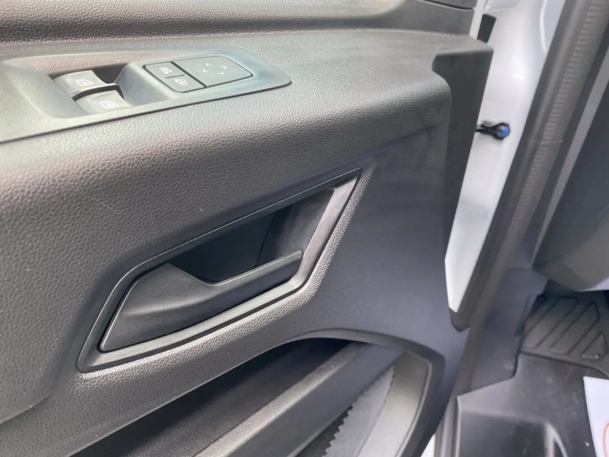 Gros plan sur la poignée intérieure et les commandes de vitre de la porte avant gauche du Renault Master blanc.