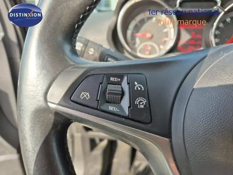 Gros plan sur le volant cuir de l'Opel Adam marron, côté gauche, avec commandes du régulateur de vitesse visibles.