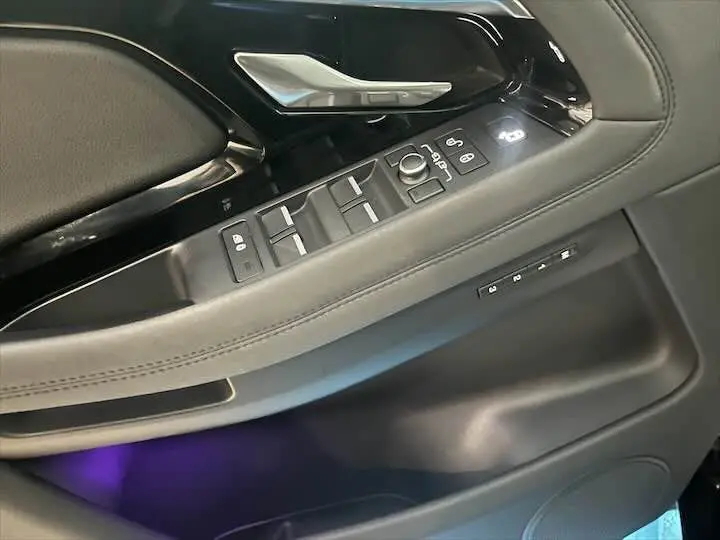 Détail de la porte côté conducteur du Range Rover Evoque noir Santorini 2020 avec commandes électriques et éclairage d'ambiance violet.