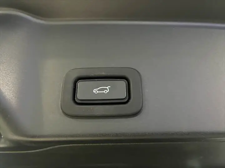 Bouton noir d'ouverture électrique du hayon avec pictogramme blanc, intérieur d'un Range Rover Evoque noir Santorini.
