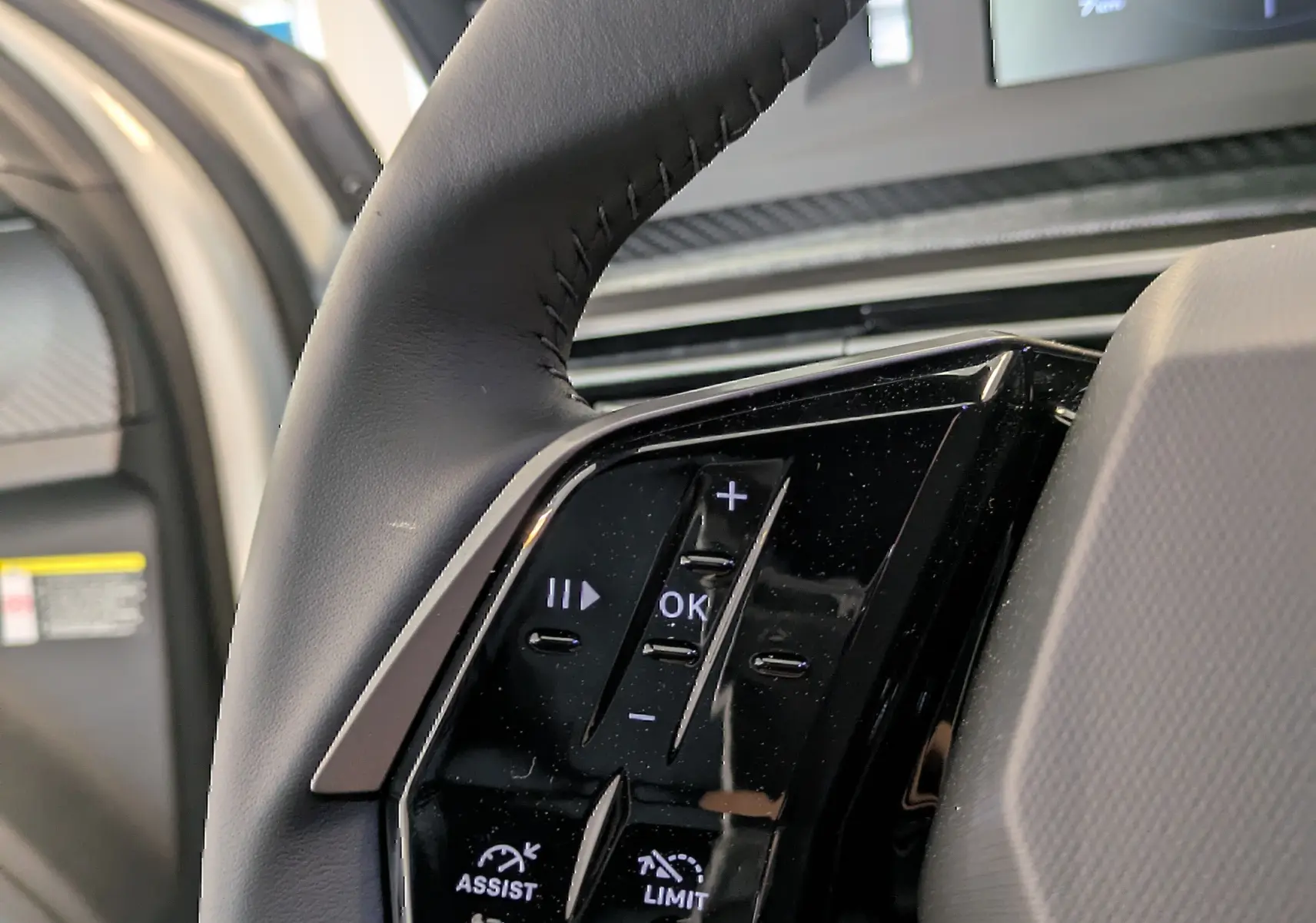 Gros plan sur les commandes du volant noir du Peugeot 5008 blanc, avec boutons d’assistance et limitation de vitesse.