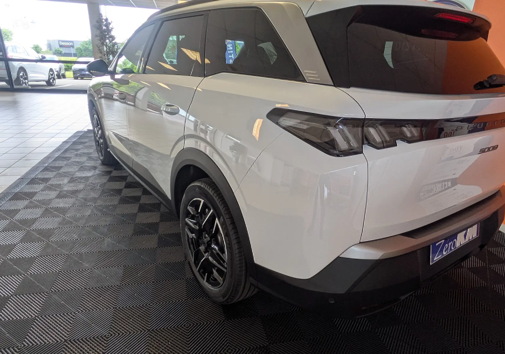 Vue 3/4 arrière droite du Peugeot 5008 blanc Okenite avec jantes alliage noires et vitres teintées en showroom.