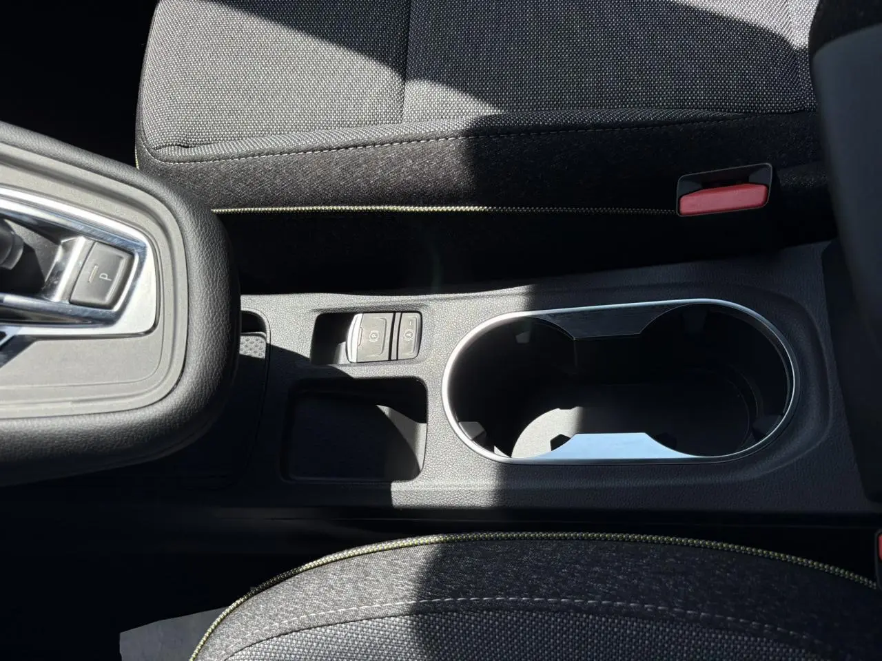 Gros plan sur la console centrale noire du Renault Captur 2025 avec porte-gobelets et commandes de frein à main électrique.