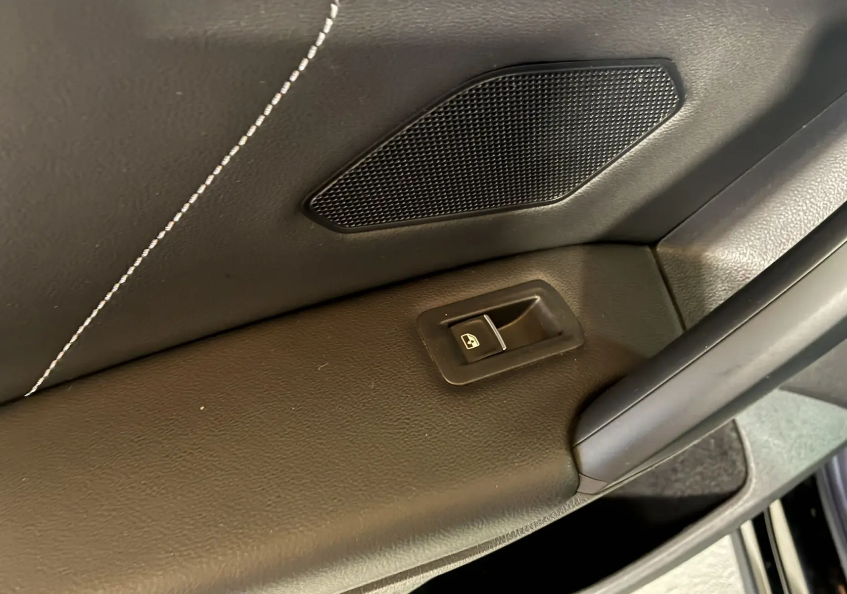 Détail de la portière intérieure noire du Volkswagen Tiguan 2022 avec bouton de commande de vitre et haut-parleur intégré.