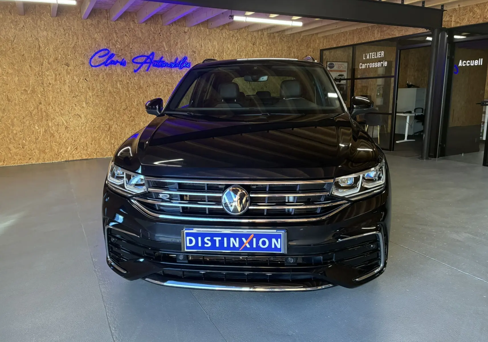 Volkswagen Tiguan noir en vue frontale dans un showroom avec logo R-Line et plaque Distinxion visible.