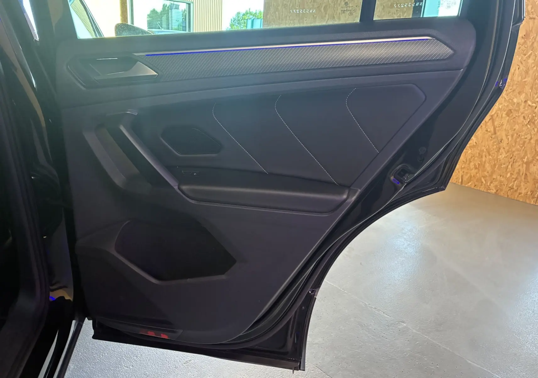 Porte arrière côté droit ouverte du Volkswagen Tiguan noir, intérieur tissu noir avec surpiqûres blanches et éclairage d'ambiance bleu.