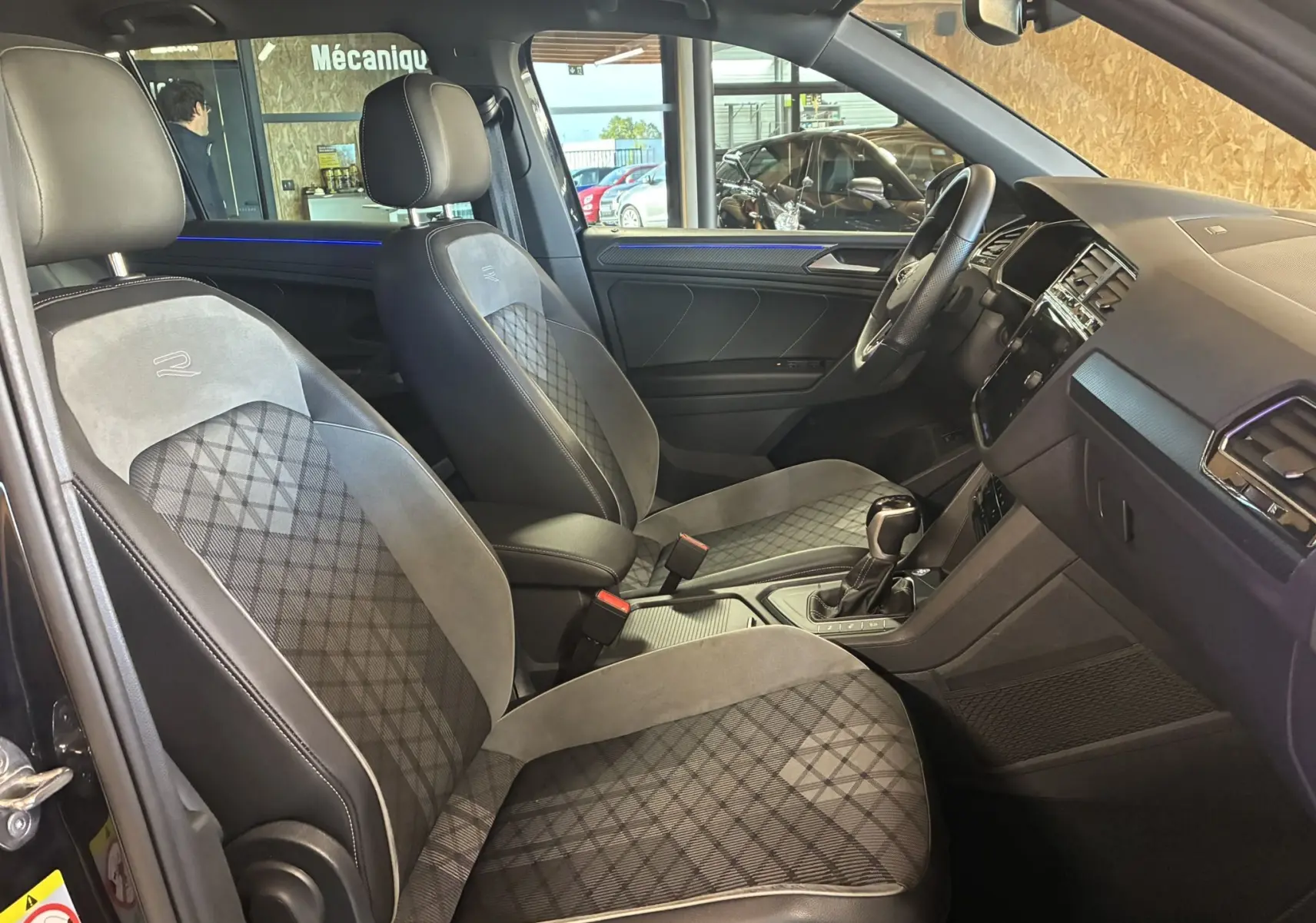 Intérieur noir du Volkswagen Tiguan 2022, vue côté conducteur, sièges sport avec surpiqûres et volant multifonctions cuir.