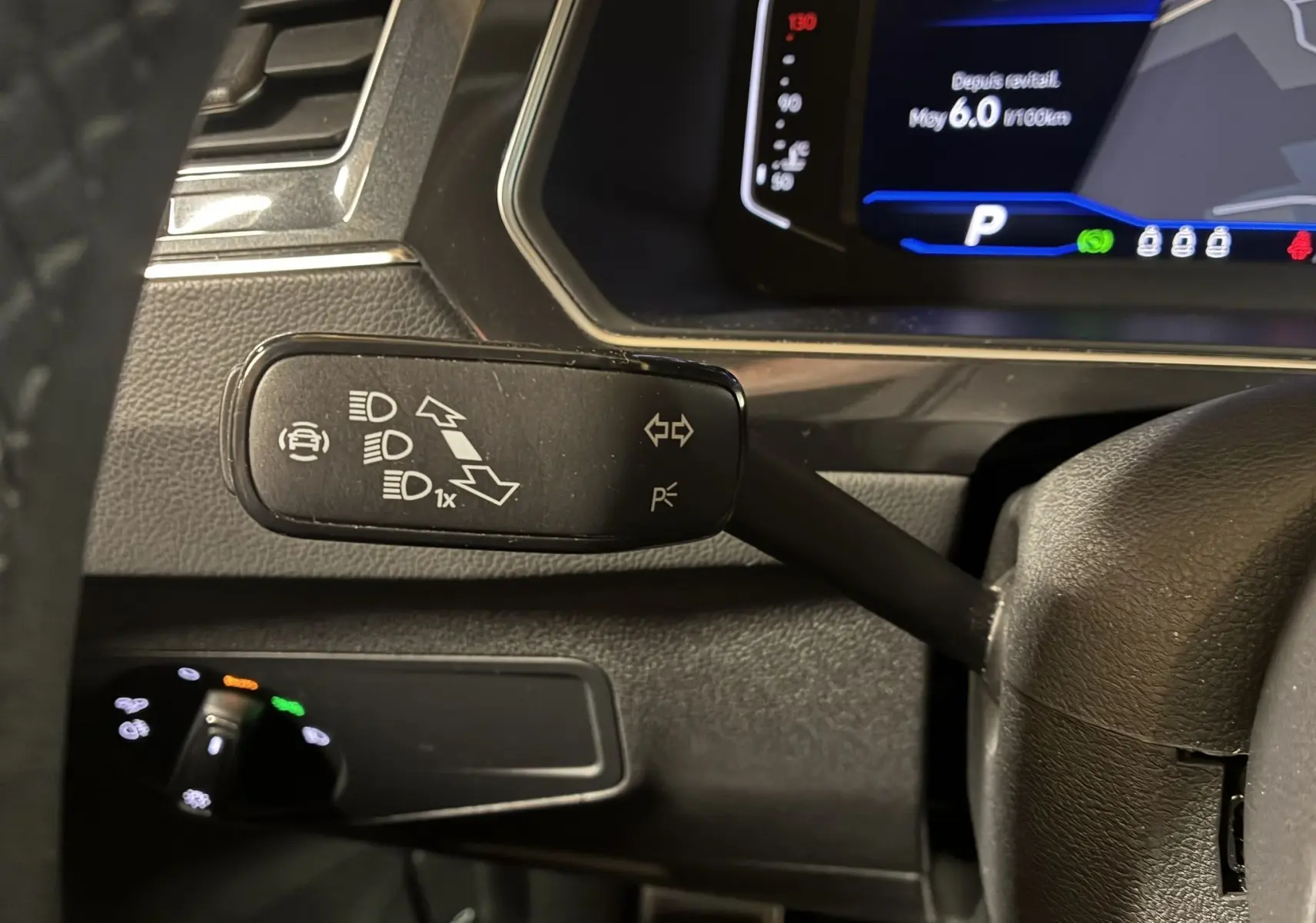 Gros plan sur le commodo gauche du volant d'un Volkswagen Tiguan noir 2022, avec tableau de bord numérique en arrière-plan.