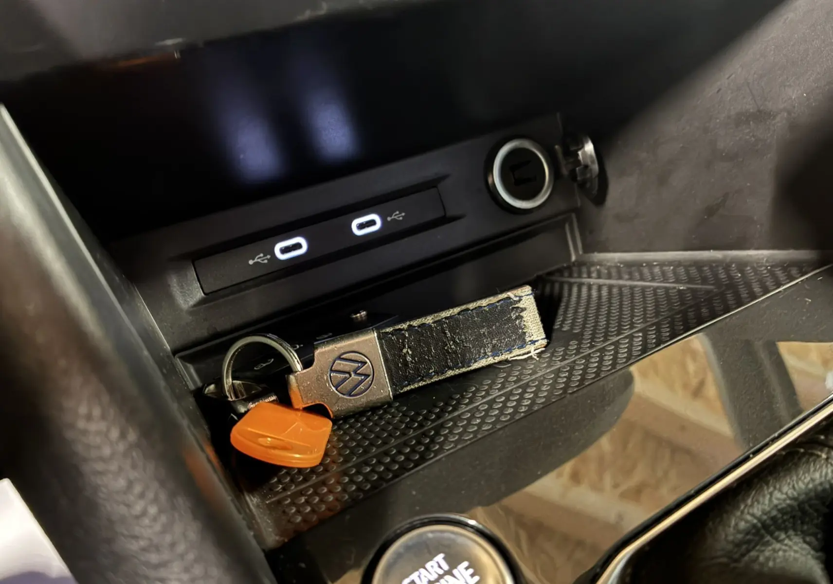 Gros plan sur la console centrale du Volkswagen Tiguan noir, avec clé VW, ports USB et bouton start engine visible.