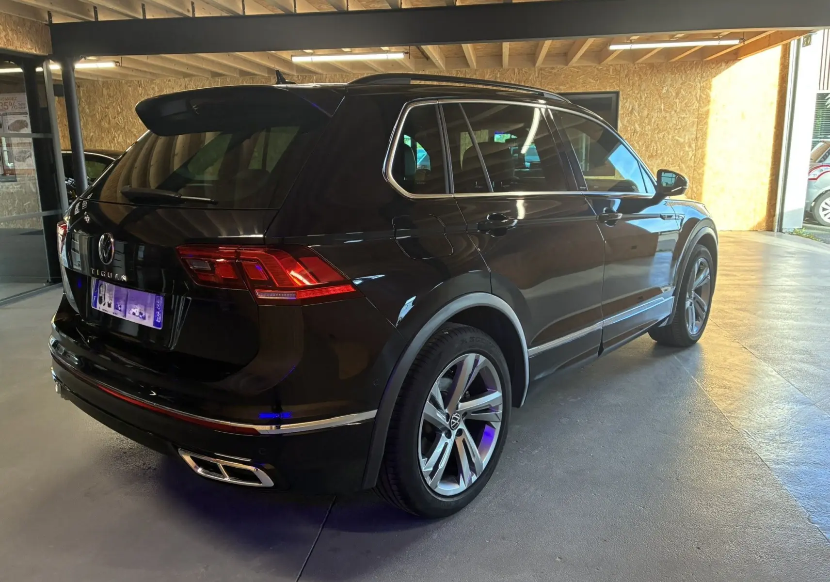 Volkswagen Tiguan noir en 3/4 arrière droit, avec jantes alu et double sortie d’échappement chromée.