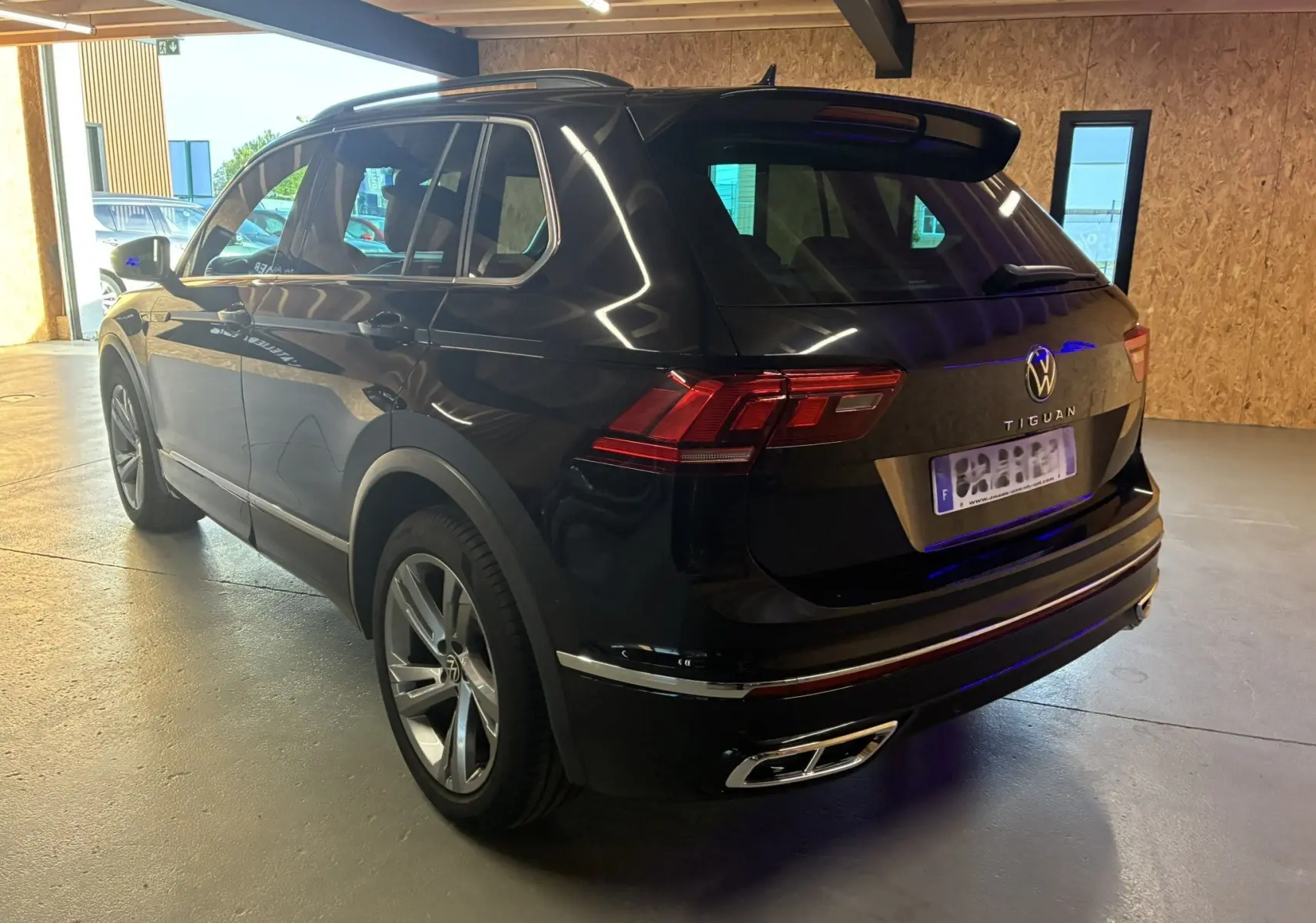 Volkswagen Tiguan noir en 3/4 arrière droit, avec jantes alu et double sortie d'échappement chromée visible en intérieur garage.