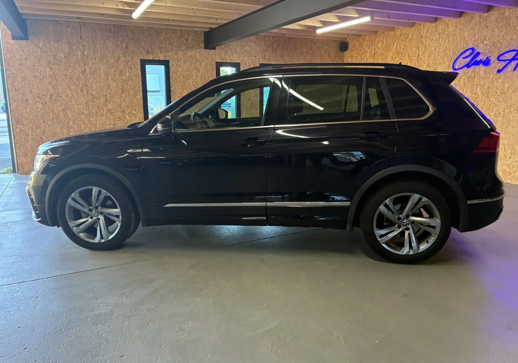 Profil côté gauche d'un Volkswagen Tiguan noir 2022 R-Line avec jantes alu, barres de toit et becquet en intérieur lumineux.