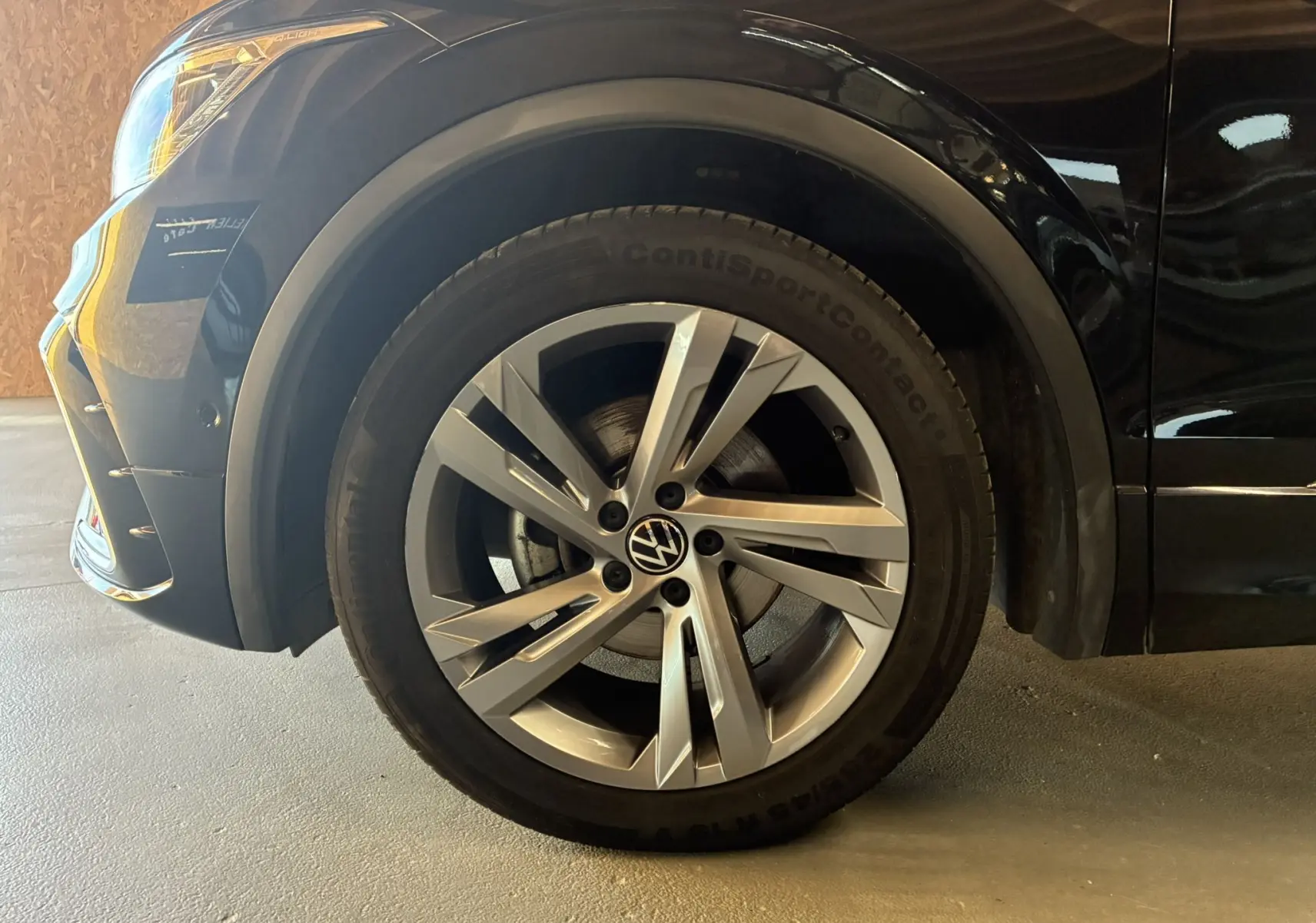 Gros plan sur la roue avant gauche en jante alu du Volkswagen Tiguan noir, avec partie du pare-chocs et phare visible.
