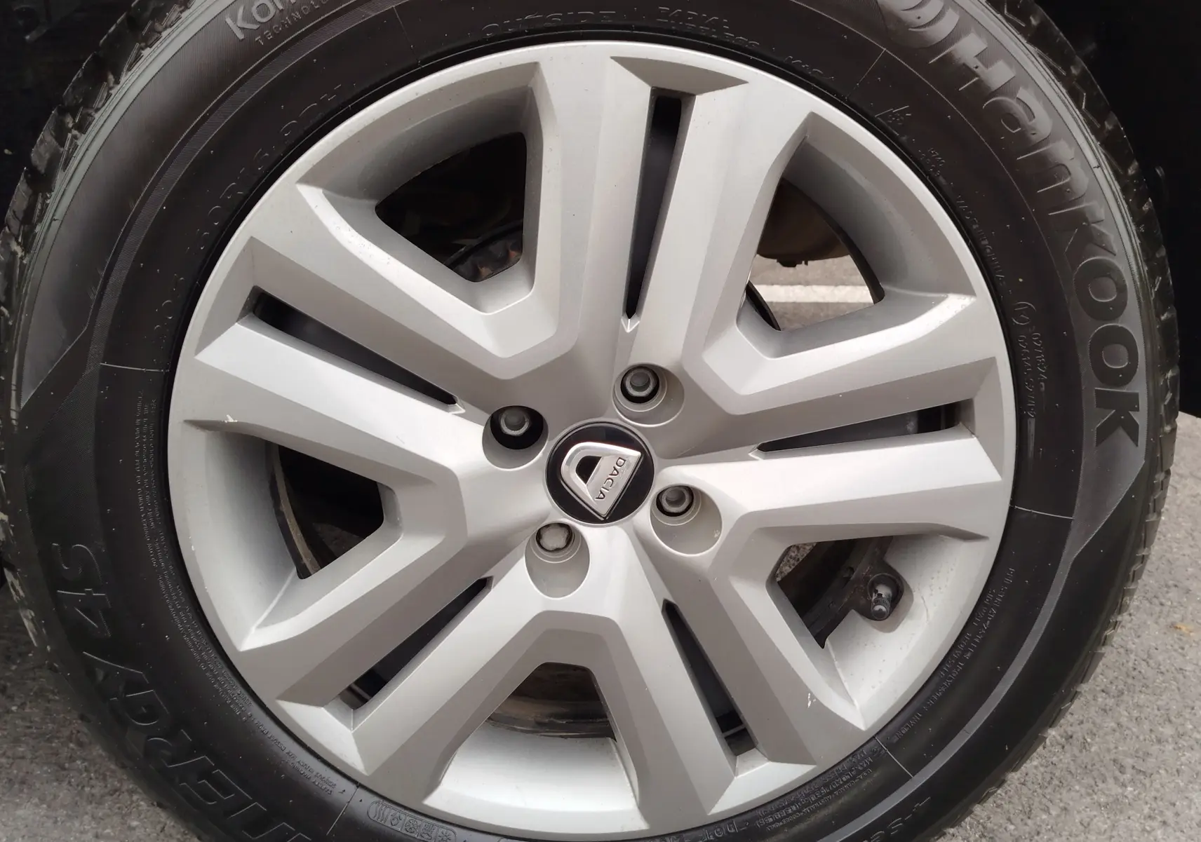 Gros plan sur la jante argentée de la roue d'une Dacia Sandero Stepway blanche, avec logo central visible.