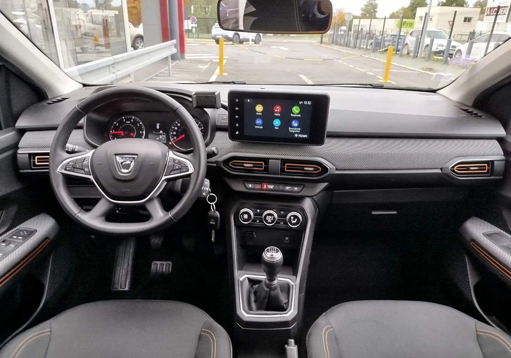 Vue intérieure avant de la Dacia Sandero Stepway 2021, tableau de bord noir avec touches orange et écran tactile central.