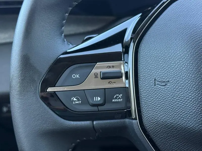 Gros plan sur les commandes gauche du volant noir du Peugeot 308 gris 1.2 Hybrid 145ch Allure 2025.