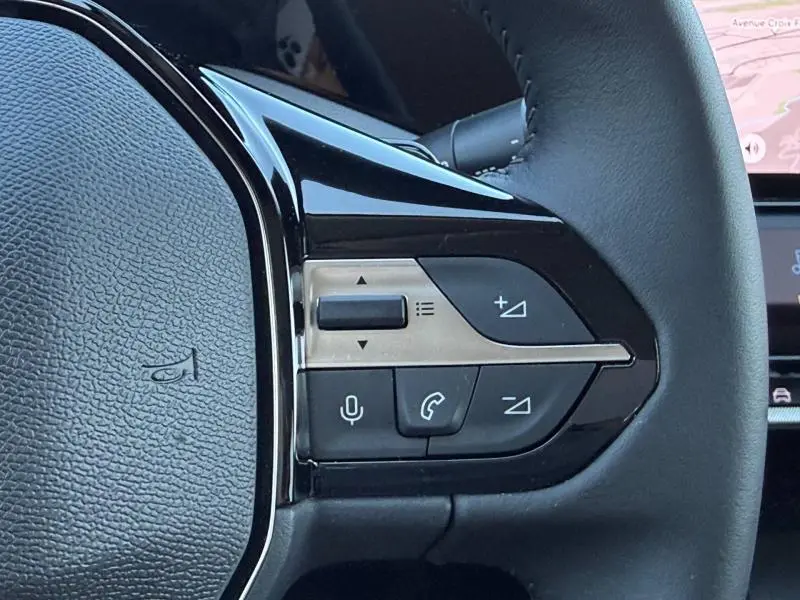 Gros plan sur les commandes noires et argentées au volant d'une Peugeot 308 gris 1.2 Hybrid 145ch Allure 2025.