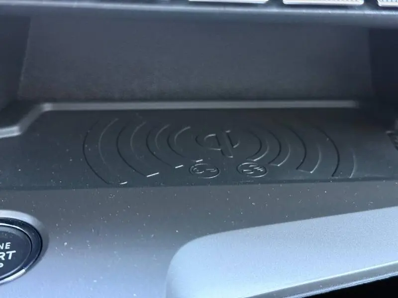 Gros plan sur le chargeur sans fil noir intégré au tableau de bord du Peugeot 308 gris 2025, avec bouton start visible.