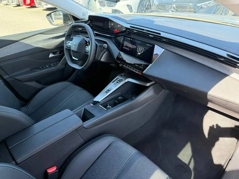 Vue intérieure côté conducteur de la Peugeot 308 1.2 Hybrid 145ch Allure 2025, avec tableau de bord moderne et sellerie noire.