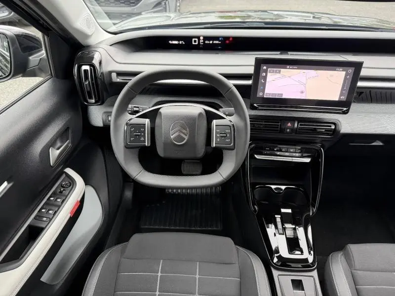 Vue intérieure frontale du poste de conduite de la Citroën C3 électrique 2025 en Noir Perla Nera, avec écran tactile et volant compact.